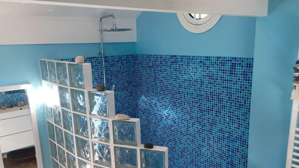 Une salle de bain avec un mur recouvert de mosaïques bleues, une douche en verre et un radiateur blanc.