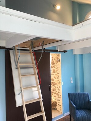 A room with a wooden ladder leaning against a wall, a door with a stone wall, and a blue-striped chair. - Beautifully renovated studio between Paris and Disneyland (Marolles-en-Brie)