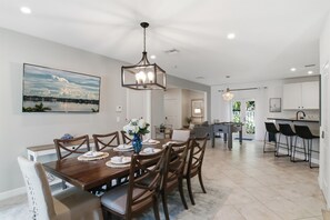 A spacious dining area with a wooden table set for six, a chandelier, and a large landscape painting on the wall.