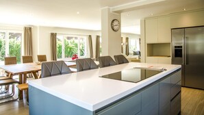 A modern kitchen with a large island, a dining area with a table and chairs, and a view of greenery outside.