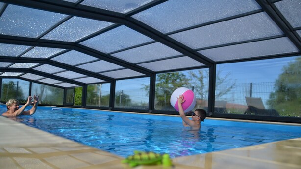 An indoor swimming pool with clear glass walls, a tiled floor, and a visible pool edge. - Gîte de l'étanchée (Châtillon-sur-Broué)