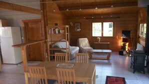 A wooden cabin interior with a dining area, a sofa, a fireplace, and a kitchen area with a refrigerator. - Gîte de l'étanchée (Châtillon-sur-Broué)
