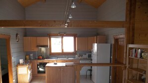 A kitchen with wooden cabinets, a central island, a microwave, a refrigerator, and a window providing natural light. - Gîte de l'étanchée (Châtillon-sur-Broué)