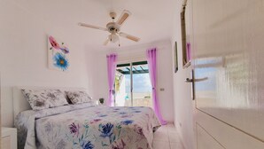A bedroom with a bed, a ceiling fan, a window with curtains, and a view of the sky.