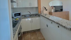 Cocina compacta con armarios blancos, encimera de granito, microondas y un lavamanos.