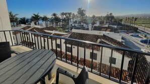 Un balcón con mesa y sillas, con vista a una calle con palmeras y edificios.