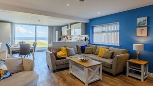 A modern living room with a sofa, coffee table, and a dining area with a view of the sea. - 3 bedroom accommodation in Reighton Gap, near Filey (Reighton Gap, near Filey)