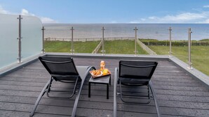 A balcony with two black lounge chairs, a small table with a tray of croissants, and a view of the sea and a wooden pier. - 3 bedroom accommodation in Reighton Gap, near Filey (Reighton Gap, near Filey)