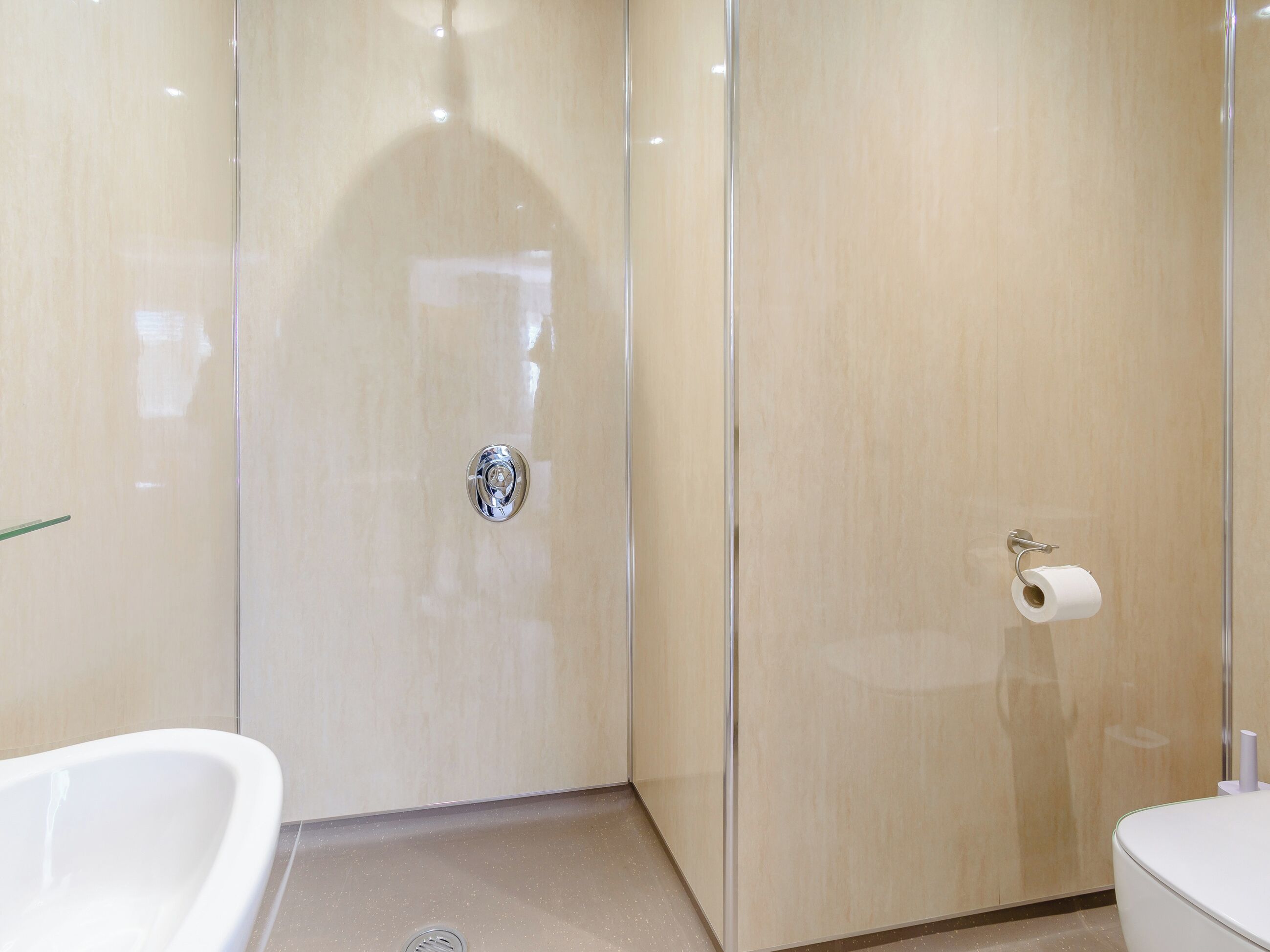 Une salle de bain moderne avec une douche à parois de verre, des toilettes dotées d’un porte-serviettes en papier et une baignoire blanche.