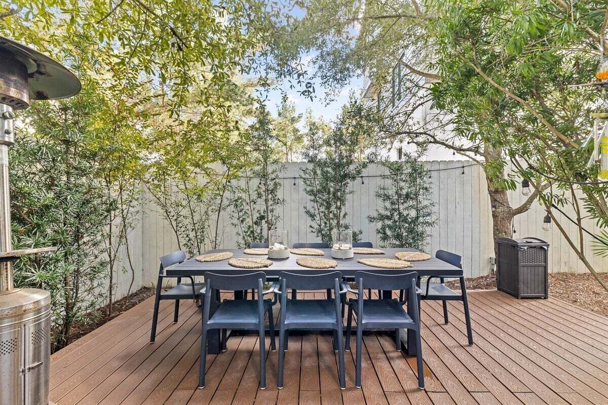 Eine Holzterrasse mit einem runden Tisch und Stühlen, umgeben von einem weißen Zaun und Bäumen.