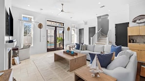 A spacious living room with a large sofa, a coffee table, and a television. There is a staircase leading to another level, and a door with glass panels.