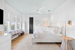 Une chambre dotée d’un grand lit, d’un banc, d’un ventilateur de plafond et offrant une vue sur l’extérieur grâce à de grandes fenêtres.