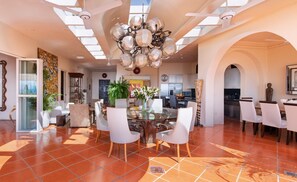 A spacious living room with a glass dining table, white chairs, and a modern chandelier.