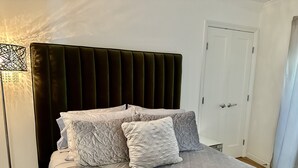 A neatly made bed with a patterned bedspread and pillows, a dark upholstered headboard, a bedside lamp, and a white door in the background. - Luxury Modern Unit on Market St - w/Private Patio - Hot tub, Fire Pit, Lounge + (SF)