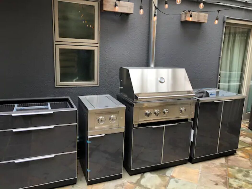 An outdoor kitchen with a stainless steel grill, a built-in oven, and a sink.