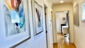 A hallway with framed abstract art, wooden flooring, and recessed lighting. - Luxury Modern Unit on Market St - w/Private Patio - Hot tub, Fire Pit, Lounge + (SF)