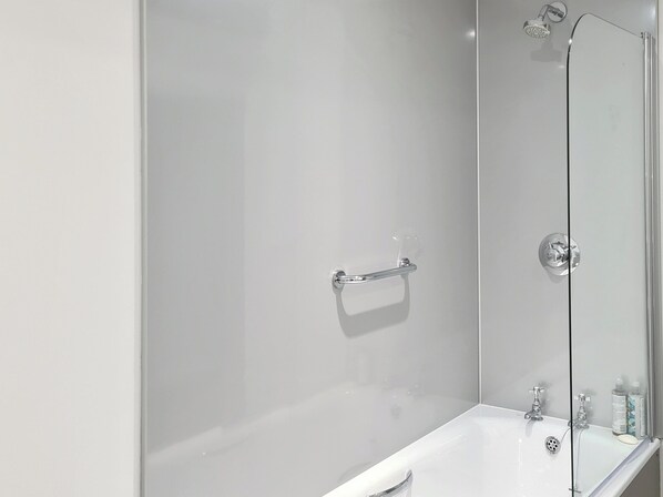 A modern bathroom with a glass shower enclosure, a white bathtub, and a glass door. - Dowie House Steading (Berwick upon Tweed)