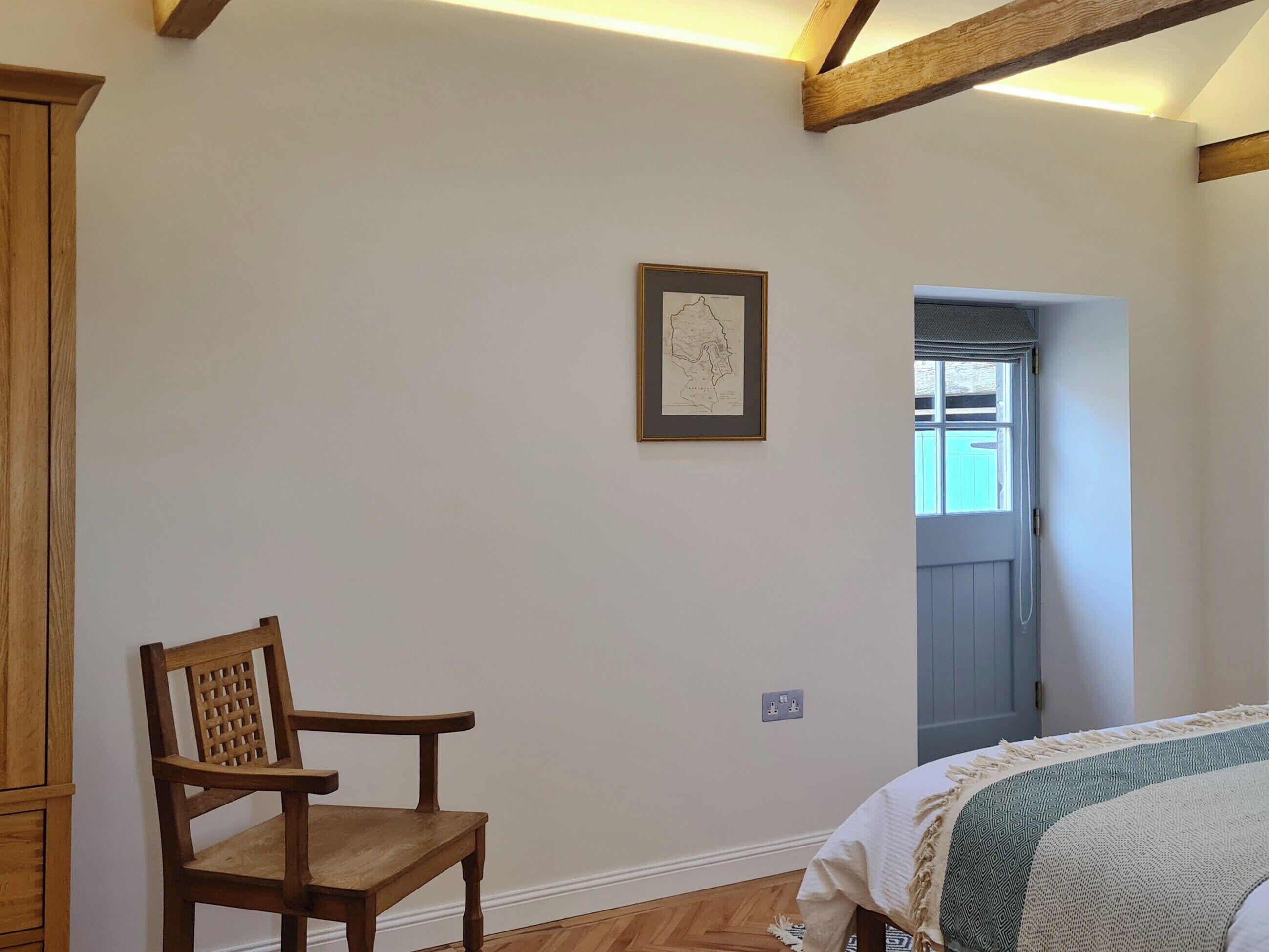 A room with a wooden chair, a bed with patterned bedding, a framed map on the wall, and a door leading to another room.