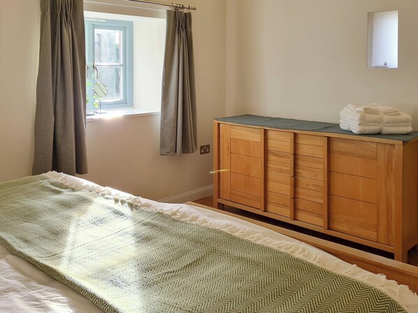 A bedroom with a bed, wooden dresser, and a window with curtains. - Dowie House Steading (Berwick upon Tweed)