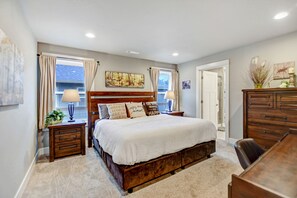 A bedroom with a large bed, wooden headboard, two bedside tables with lamps, a dresser, and a painting on the wall. - Drift Away - A beautiful River front home in Southern Oregon (Gold Hill)