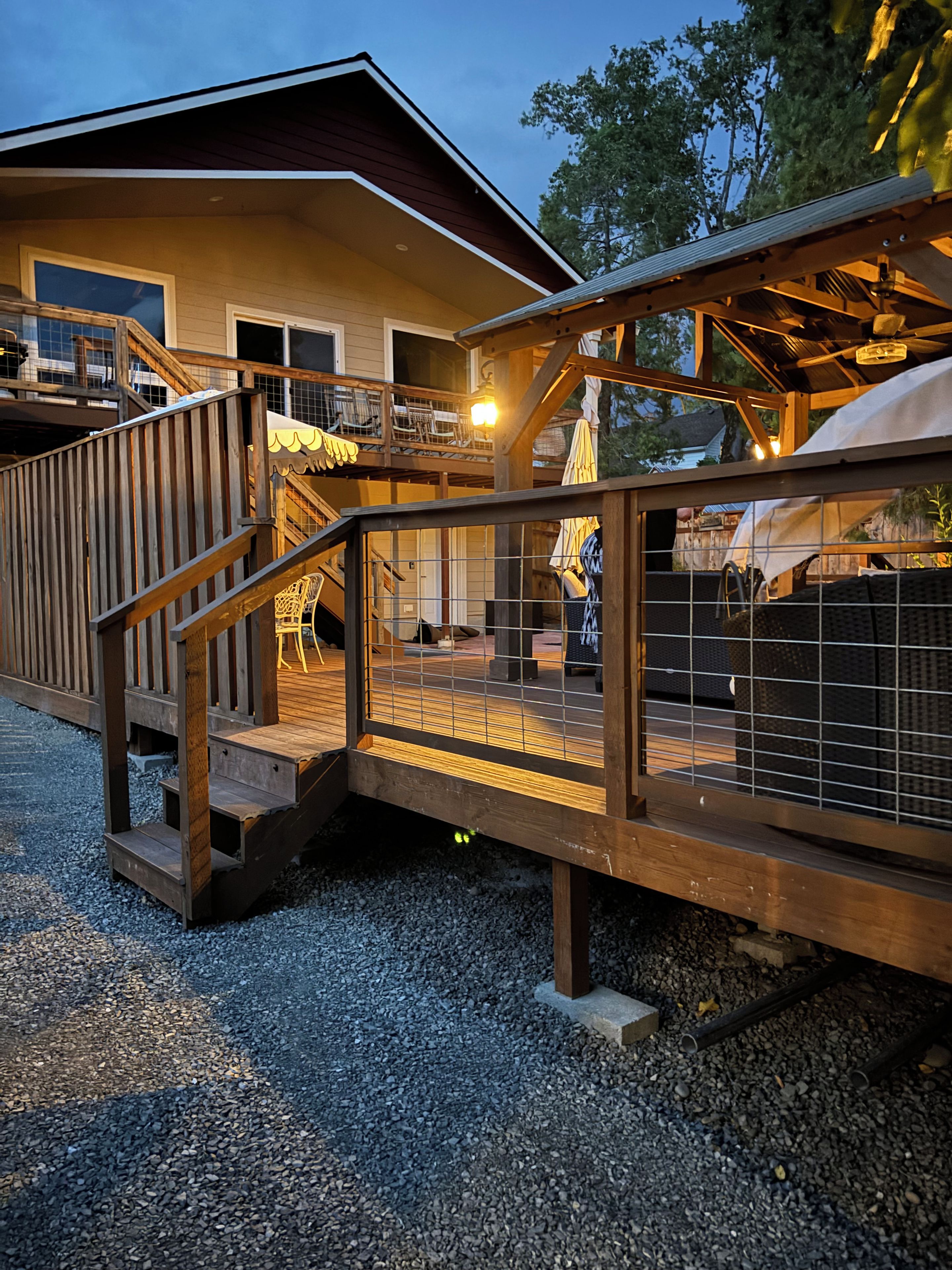 Une terrasse en bois, dotée d’une rambarde, qui mène à un espace extérieur abrité, aménagé avec des chaises et des parasols.
