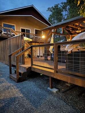 A wooden deck with a railing leading to a covered outdoor area with chairs and umbrellas.