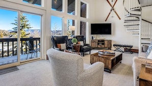 A spacious living room with large windows, a fireplace, a TV, and a staircase. - 🏔️Ski-In, Ski-Out~Hot Tub~Top Floor~Interlude 301🏔️ (Snowmass Village)