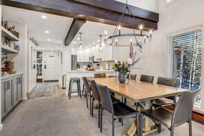 A modern dining area with a wooden table, black chairs, and a chandelier.