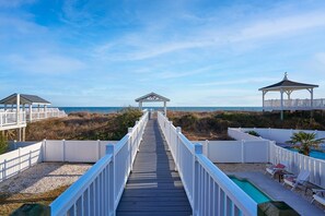 A wooden boardwalk leading to a gazebo, a pool area, and beach views. - Dog Friendly Oceanfront Beach Cottage Private Pool (Ocean Isle Beach)