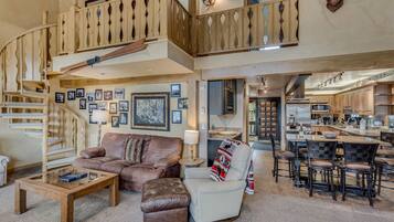 A spacious living area with a wooden staircase, a comfortable sofa, a coffee table, and a dining area with bar stools.