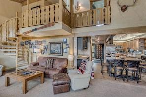 A spacious living area with a wooden staircase, a comfortable sofa, a coffee table, and a dining area with bar stools.
