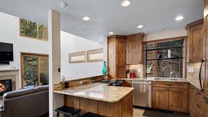 A modern kitchen with wooden cabinets, a granite countertop, and a built-in island with stools. - Casa Del Sol (Vail)