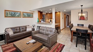 A spacious living room with a large brown leather sofa, a coffee table, and a dining area with a wooden table and chairs. - Casa Del Sol (Vail)