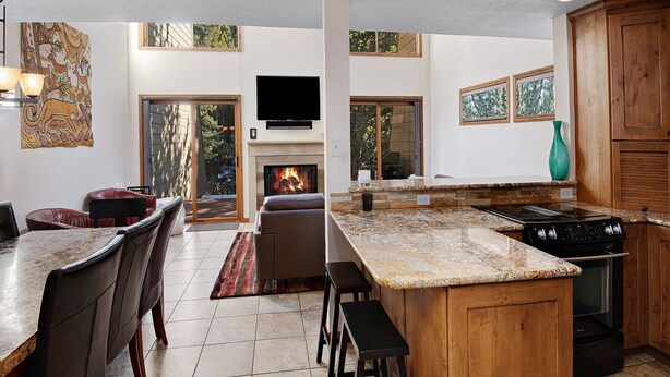 A modern kitchen with a large island, a fireplace, and a dining area with leather chairs. - Casa Del Sol (Vail)
