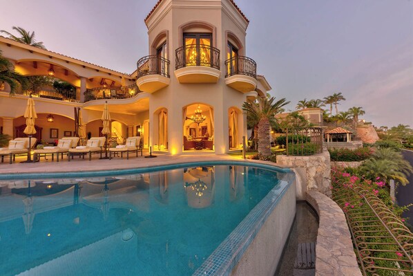A luxurious hotel with a swimming pool, outdoor seating, and a well-lit interior.