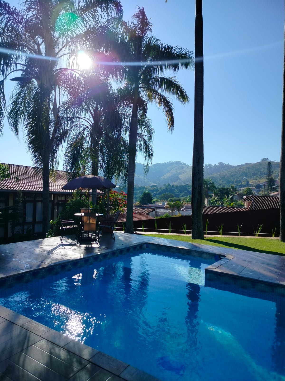 Ein Pool mit Bergblick, umgeben von Palmen und einer Terrasse mit Gartenmöbeln.