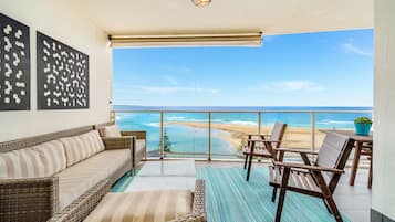 A balcony with wicker furniture, a view of the beach, and a potted plant.