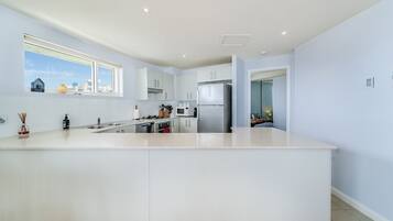 A modern kitchen with a central island, white cabinetry, and a view of the city through a window.
