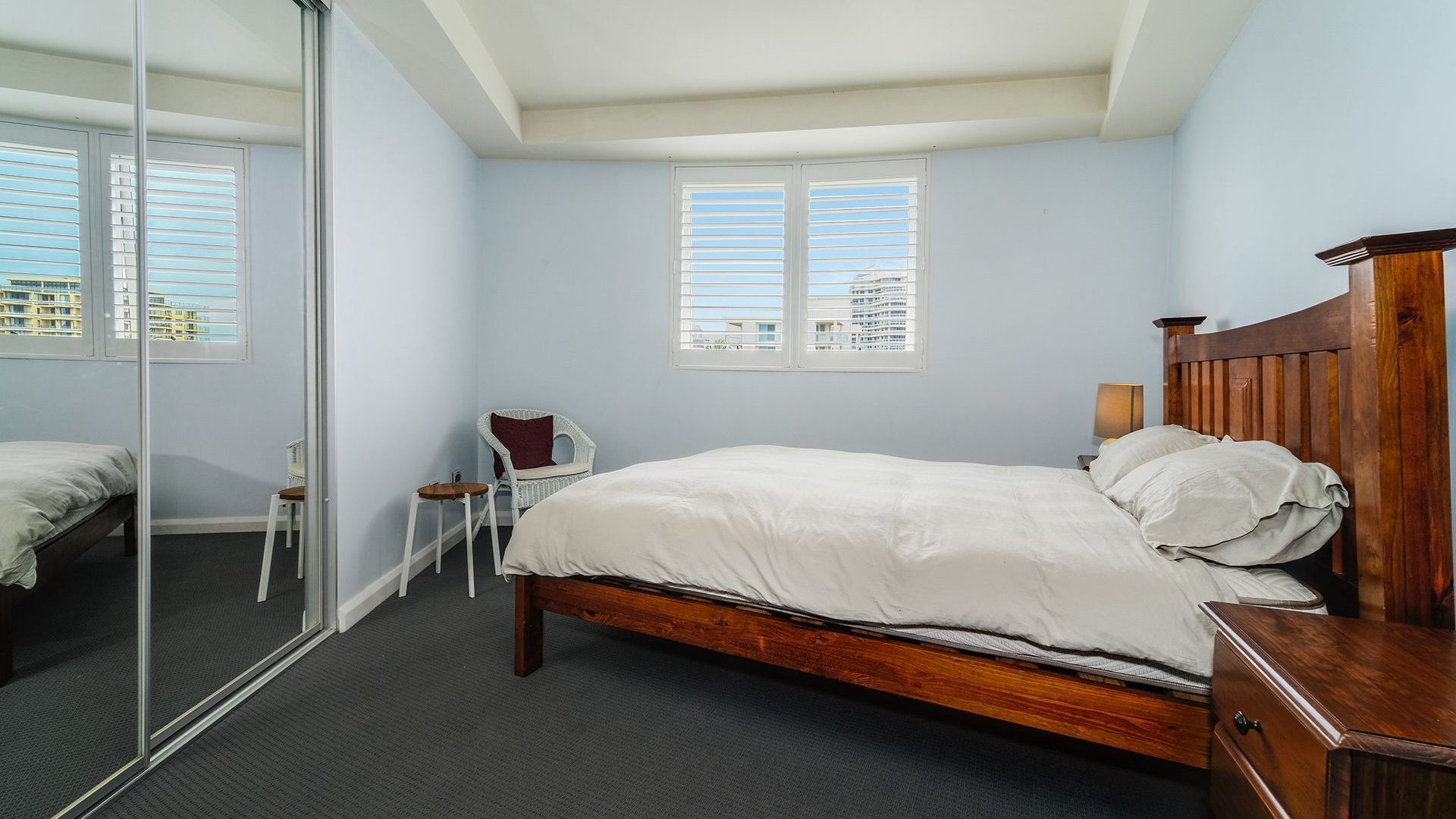 A bedroom with a wooden bed, a chair, a small table, and a mirror.