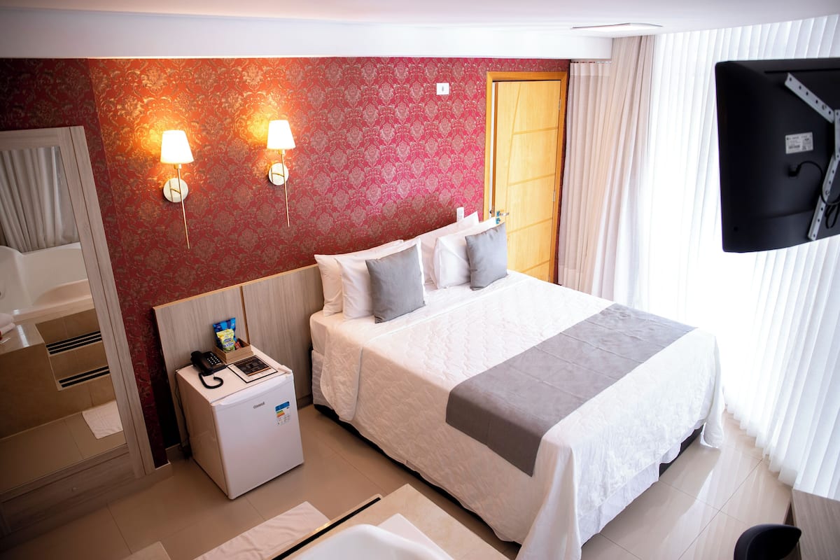 Ein Hotelzimmer mit einem Bett, einem Schreibtisch mit Telefon und einem kleinen Gerät, zwei Wandlampen und einem Fernseher an der Wand.