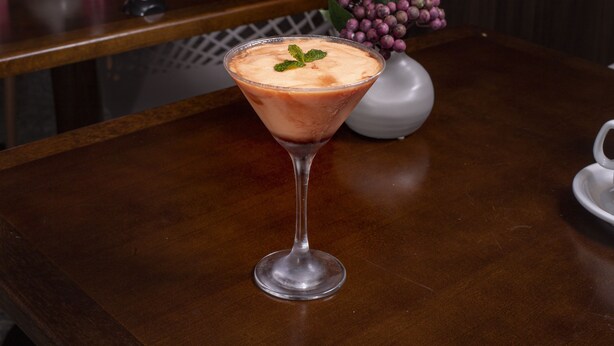 Een martini glas met een roze drankje op een houten tafel.