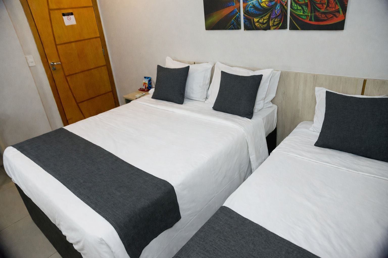 A hotel room with two single beds, a wooden wardrobe, and a small table with a remote control.