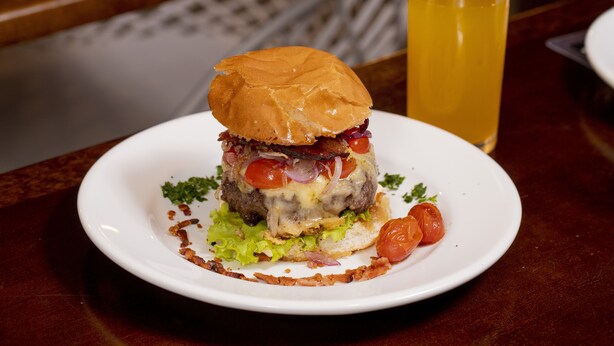 Un hamburger avec de la laitue, des tomates et du bacon, servi sur une assiette blanche.