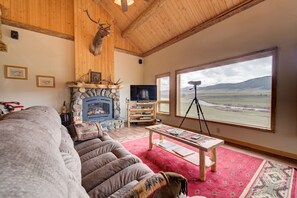 A cozy living room with a stone fireplace, a large window with a view of the countryside, a comfortable sofa, and a television.