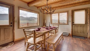 Une salle à manger en bois avec une grande table, des bancs et un lustre. De grandes fenêtres offrent une vue sur les montagnes.