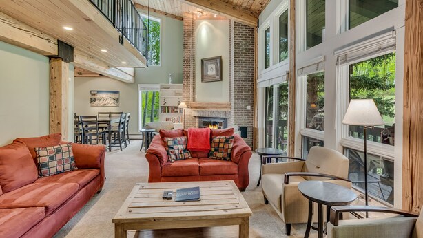 Amplia sala de estar con techos altos, chimenea y ventanas grandes que ofrecen vistas al exterior.