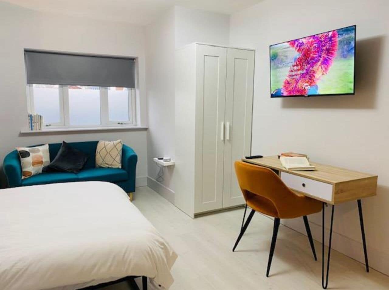 A bedroom with a bed, a desk, a chair, a wardrobe, and a TV on the wall.