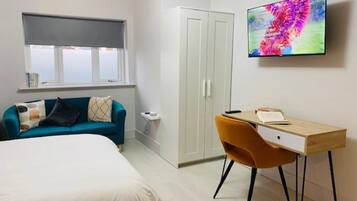 A bedroom with a bed, a desk, a chair, a wardrobe, and a TV on the wall.