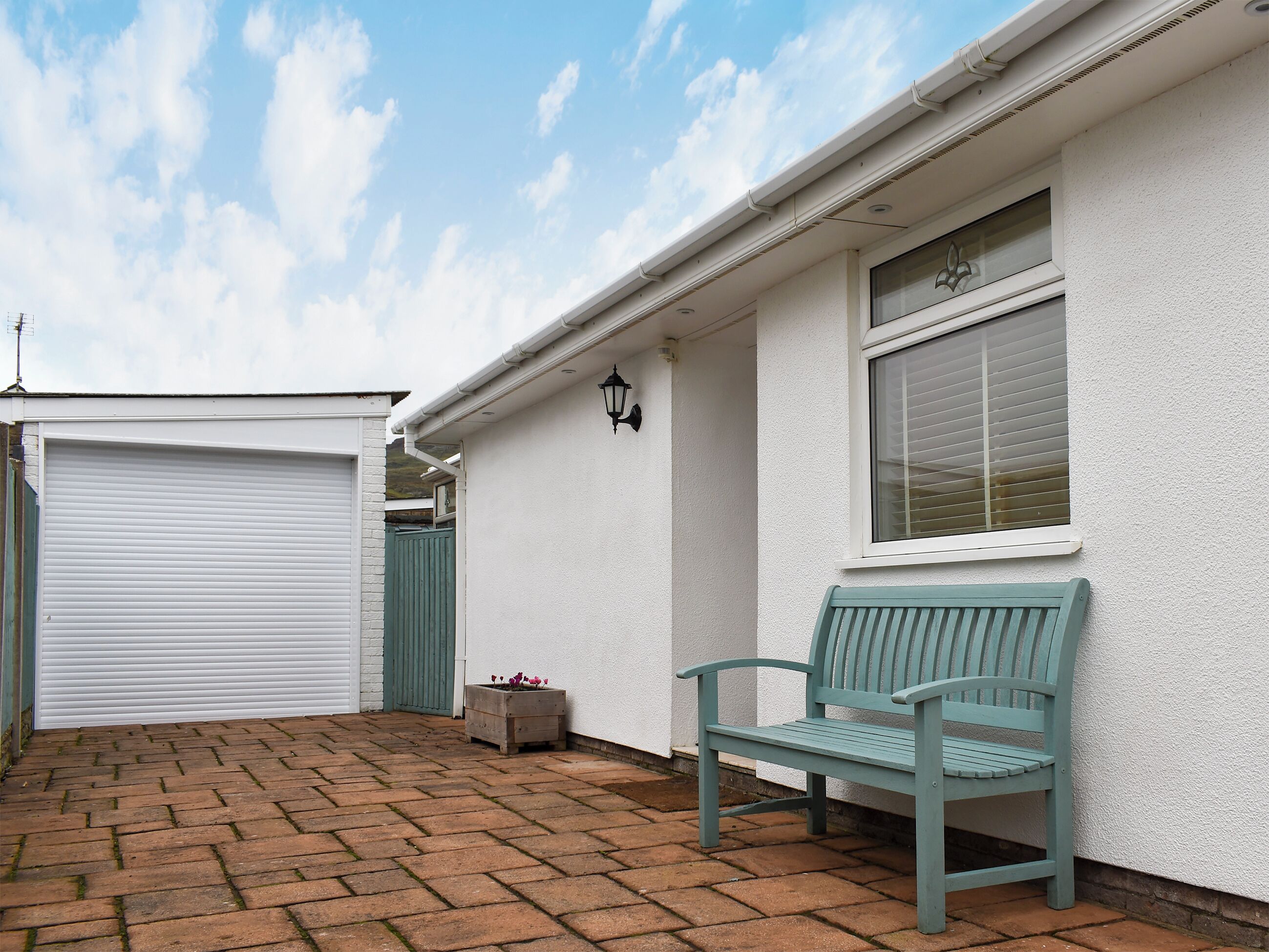 A building with a closed garage door, a bench, a potted plant, and a window with blinds.