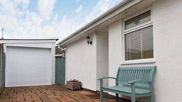 A building with a closed garage door, a bench, a potted plant, and a window with blinds.